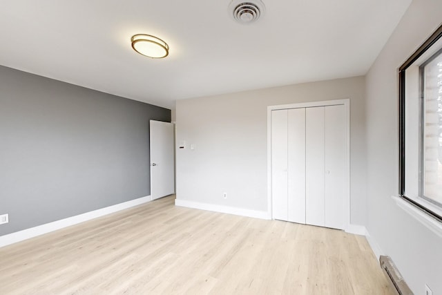 unfurnished bedroom with light wood-style floors, a baseboard radiator, visible vents, and baseboards