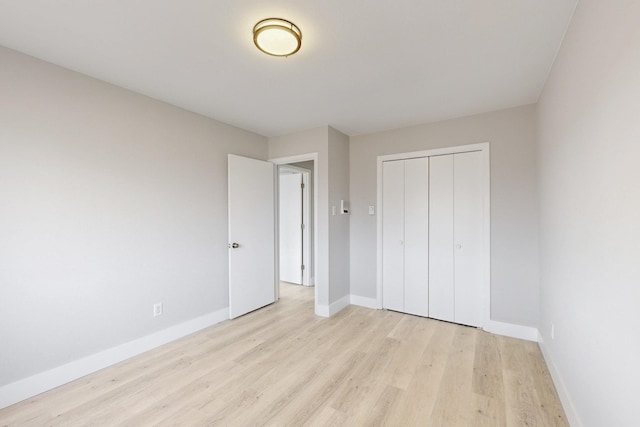 unfurnished bedroom featuring light wood-style floors, baseboards, and a closet