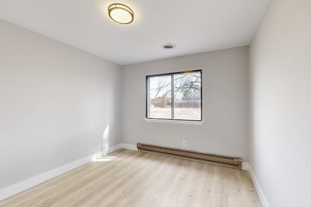 empty room featuring a baseboard heating unit, light wood-type flooring, visible vents, and baseboards