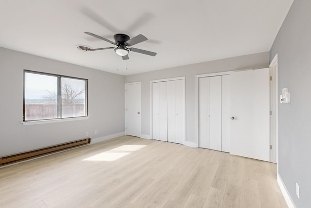 unfurnished bedroom featuring light wood finished floors, multiple closets, visible vents, a baseboard heating unit, and baseboards