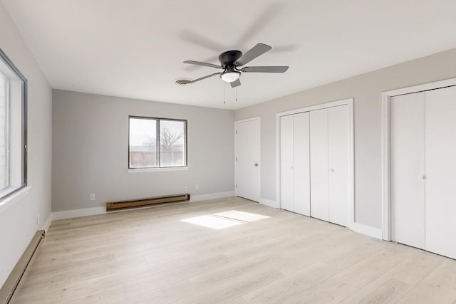 unfurnished bedroom with visible vents, a baseboard radiator, wood finished floors, a baseboard heating unit, and two closets