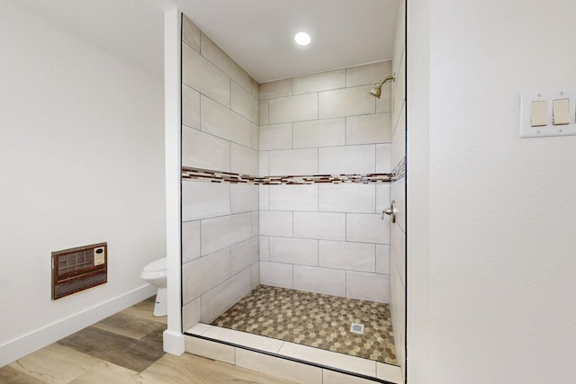 bathroom with heating unit, toilet, wood finished floors, tiled shower, and baseboards