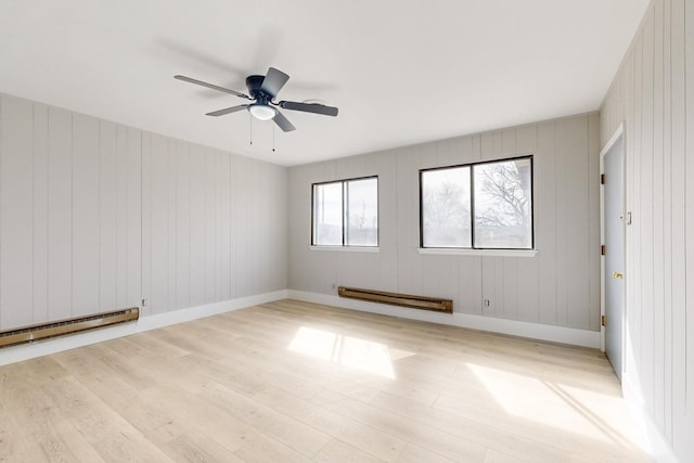 spare room featuring a baseboard heating unit, light wood-type flooring, ceiling fan, and baseboards