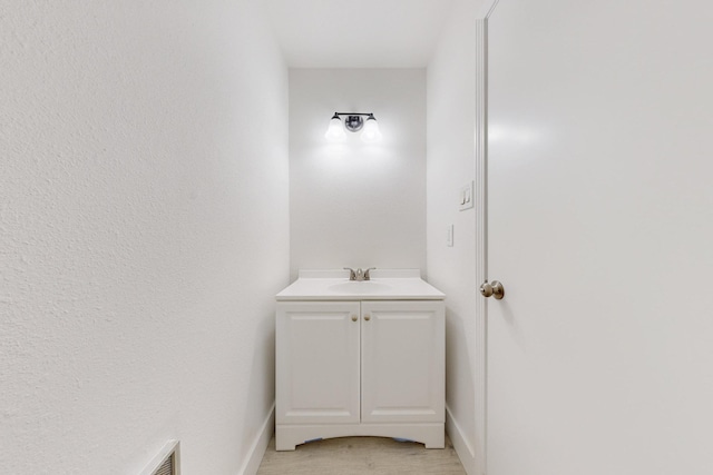 bathroom with visible vents, vanity, baseboards, and wood finished floors