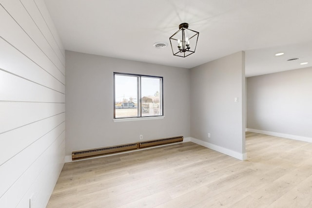 spare room with a notable chandelier, visible vents, light wood-style flooring, baseboard heating, and baseboards