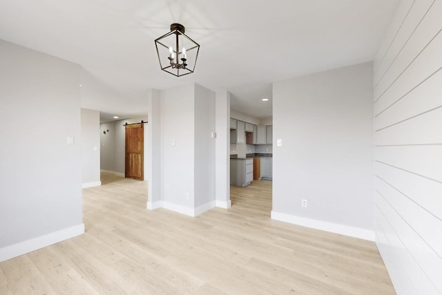 unfurnished dining area featuring light wood-style floors, a barn door, baseboards, and a chandelier