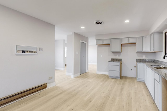 kitchen with a baseboard radiator, light wood-style flooring, gray cabinetry, a sink, and visible vents