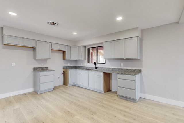 kitchen featuring visible vents, gray cabinetry, light wood-style floors, a sink, and baseboards