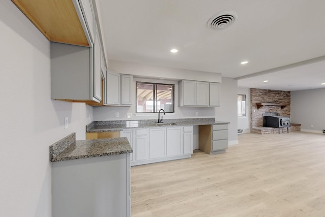 kitchen with stone counters, light wood finished floors, visible vents, open floor plan, and a sink