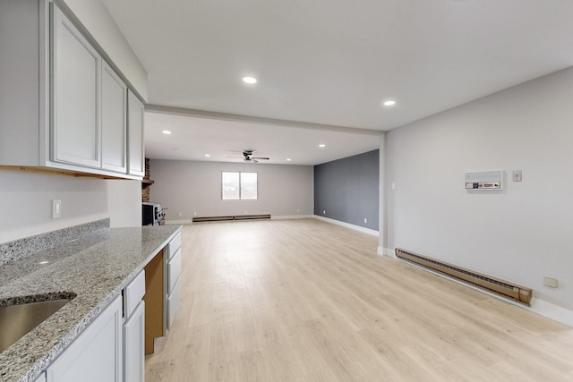 kitchen featuring a ceiling fan, a baseboard radiator, light stone counters, light wood-type flooring, and a baseboard heating unit