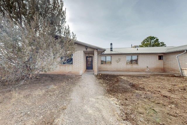 view of front of property featuring brick siding, metal roof, dirt driveway, and a patio