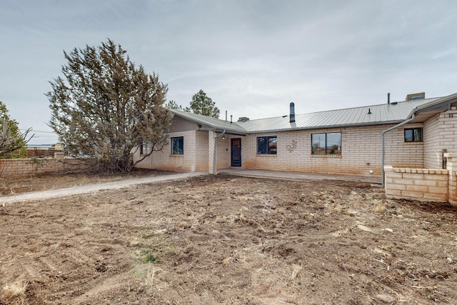 back of house featuring metal roof, brick siding, and a patio area