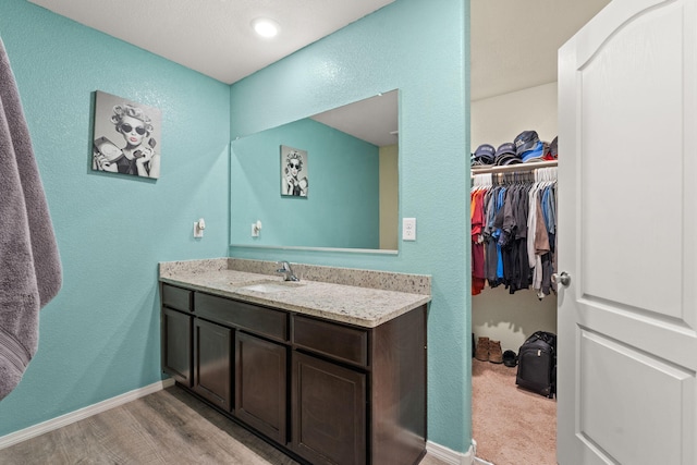 bathroom featuring wood finished floors, a walk in closet, vanity, and baseboards