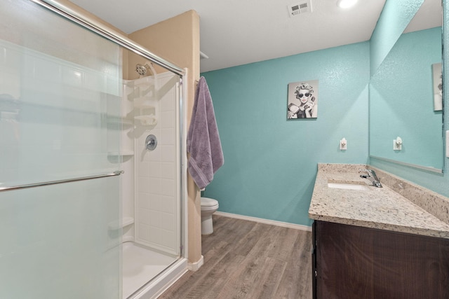 bathroom with visible vents, toilet, vanity, a shower stall, and wood finished floors