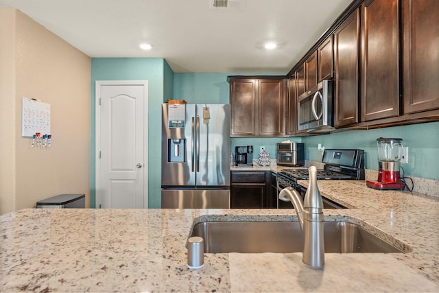 kitchen featuring stainless steel appliances, visible vents, dark brown cabinetry, a sink, and light stone countertops