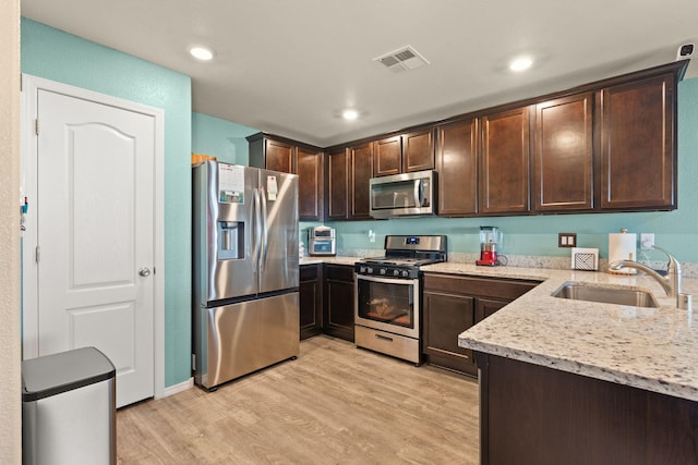 kitchen with stainless steel appliances, a sink, light stone counters, and dark brown cabinets