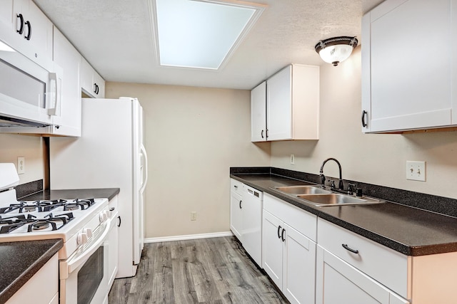 kitchen with dark countertops, white appliances, white cabinets, and a sink