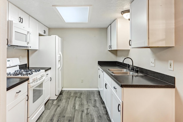 kitchen featuring white appliances, a sink, white cabinetry, light wood-type flooring, and dark countertops