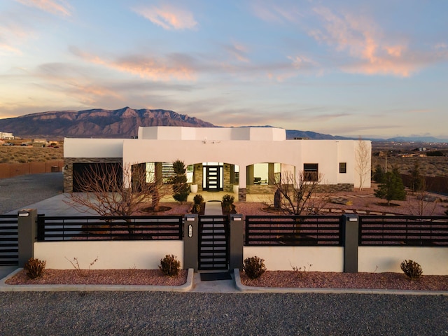 southwest-style home featuring a fenced front yard, a gate, a mountain view, and stucco siding