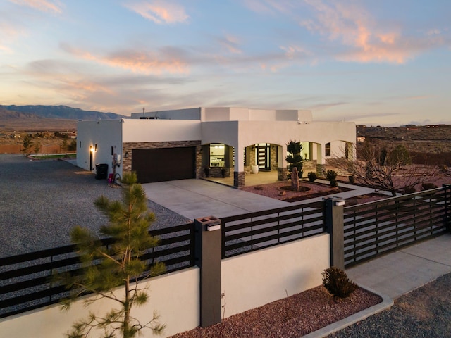 view of front of property featuring a fenced front yard, a garage, stone siding, concrete driveway, and stucco siding