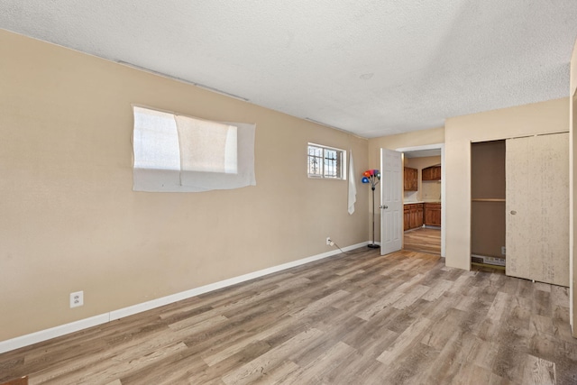 empty room with light wood-style flooring, baseboards, and a textured ceiling