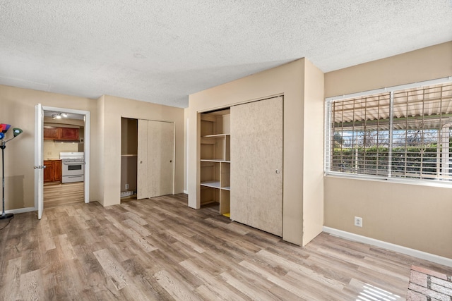 unfurnished bedroom featuring light wood-style floors, a textured ceiling, baseboards, and two closets