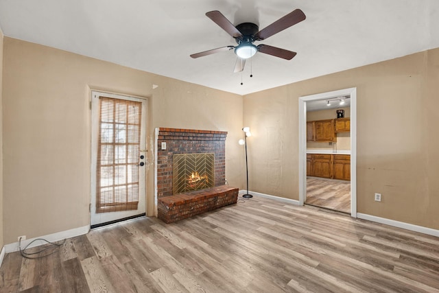 unfurnished living room featuring light wood-style floors, a brick fireplace, baseboards, and a ceiling fan