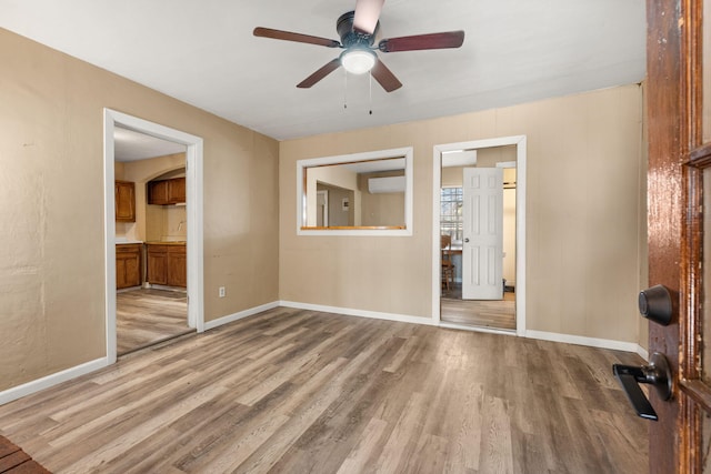 empty room with a ceiling fan, light wood-type flooring, a wall mounted air conditioner, and baseboards