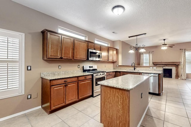 kitchen featuring light stone counters, brown cabinets, stainless steel appliances, hanging light fixtures, and a peninsula