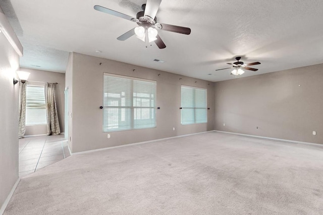 empty room with light carpet, a textured ceiling, visible vents, and baseboards