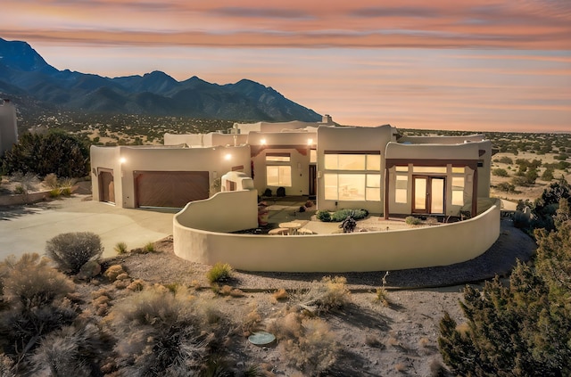 pueblo revival-style home with a garage, driveway, a mountain view, and stucco siding