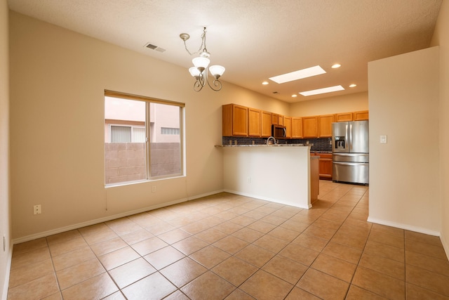 kitchen featuring a skylight, pendant lighting, light tile patterned floors, stainless steel appliances, and backsplash