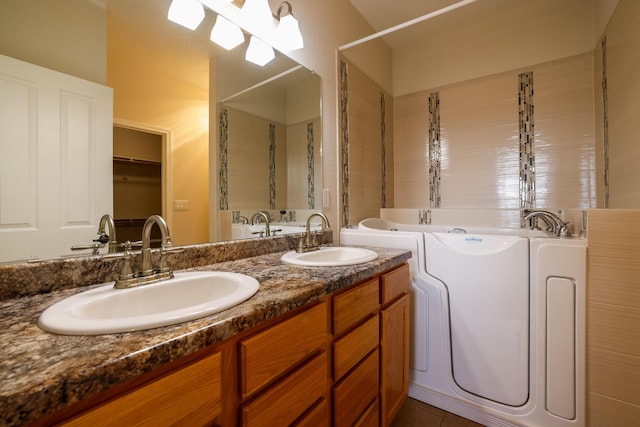 full bathroom with double vanity, a spacious closet, a sink, and a bath