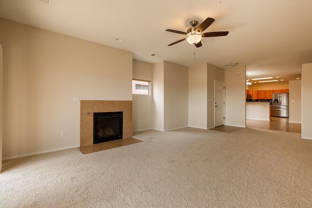 unfurnished living room featuring light carpet, a tiled fireplace, a ceiling fan, and baseboards