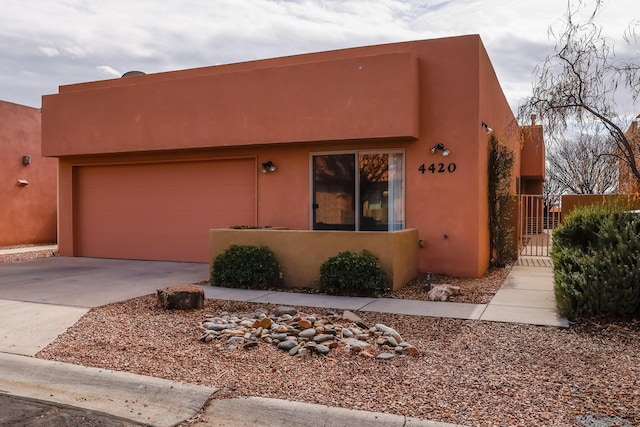 pueblo-style home with concrete driveway, an attached garage, and stucco siding