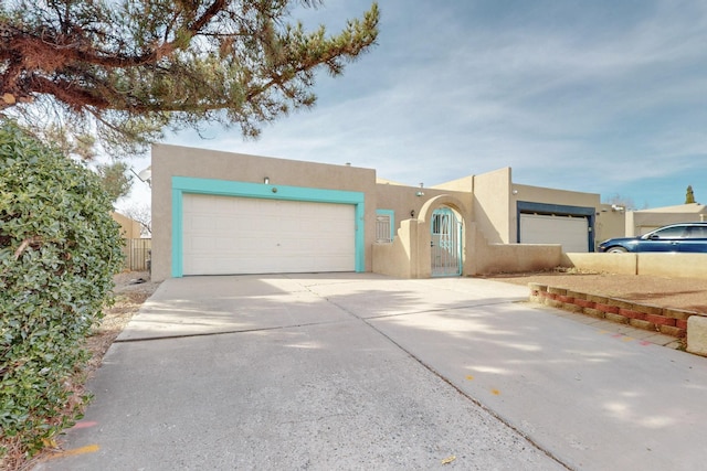 pueblo revival-style home with driveway, an attached garage, and stucco siding