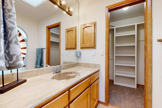 bathroom featuring a walk in closet, vanity, baseboards, and a textured ceiling