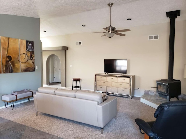 carpeted living area with arched walkways, a wood stove, visible vents, and a ceiling fan