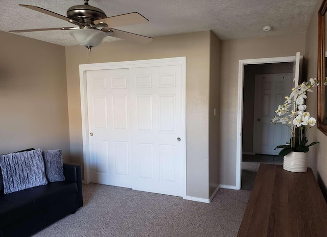 interior space featuring a textured ceiling, a ceiling fan, baseboards, a closet, and dark colored carpet