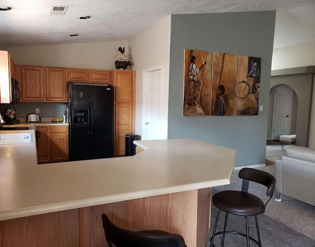 kitchen featuring visible vents, light countertops, black appliances, a peninsula, and a kitchen breakfast bar