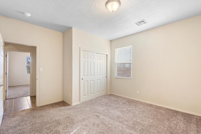 1735 Garden Way SW, Albuquerque, NM 87105 - unfurnished bedroom with light tile patterned floors, visible vents, light colored carpet, a textured ceiling, and a closet