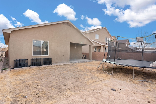 back of house featuring a trampoline, a patio area, fence, and stucco siding