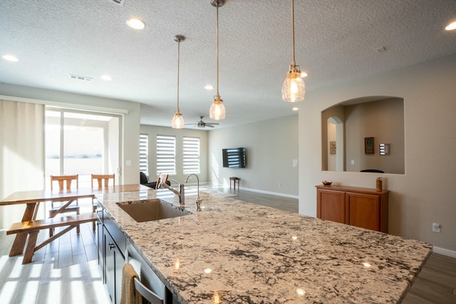 kitchen featuring a kitchen island with sink, a sink, visible vents, hanging light fixtures, and light wood-type flooring