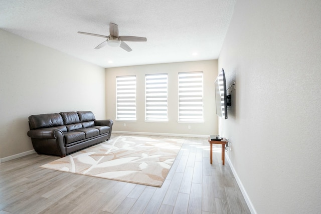 living area with ceiling fan, light wood finished floors, a textured ceiling, and baseboards