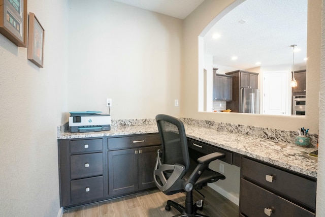 office area with arched walkways, built in study area, and light wood finished floors