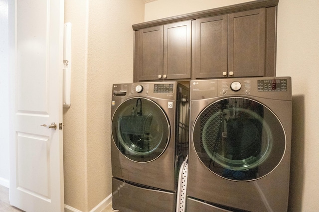 clothes washing area with washing machine and clothes dryer, cabinet space, and baseboards