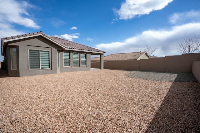 rear view of property with a fenced backyard, a tile roof, a patio, and stucco siding