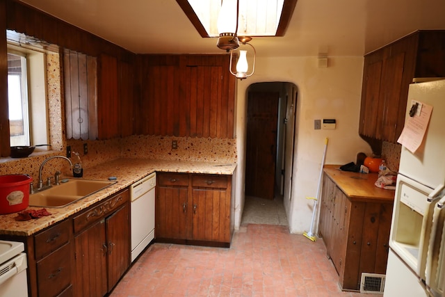 kitchen featuring arched walkways, brick floor, white appliances, a sink, and visible vents