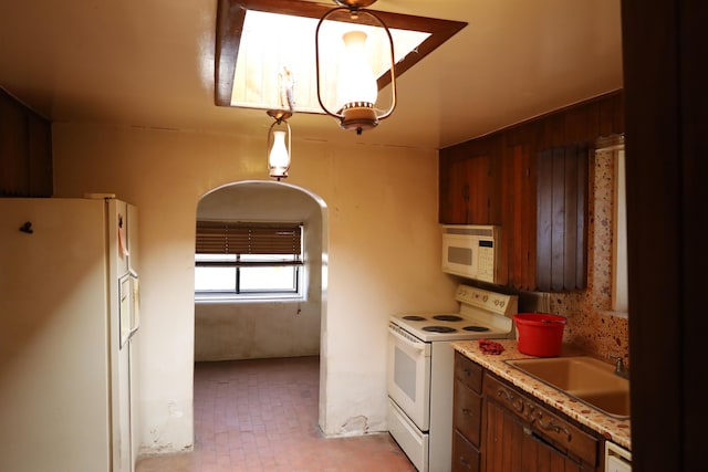 kitchen with arched walkways, brick floor, white appliances, a sink, and light countertops