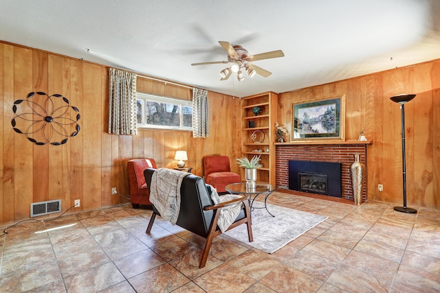 living area with wood walls, a fireplace, a ceiling fan, visible vents, and built in features